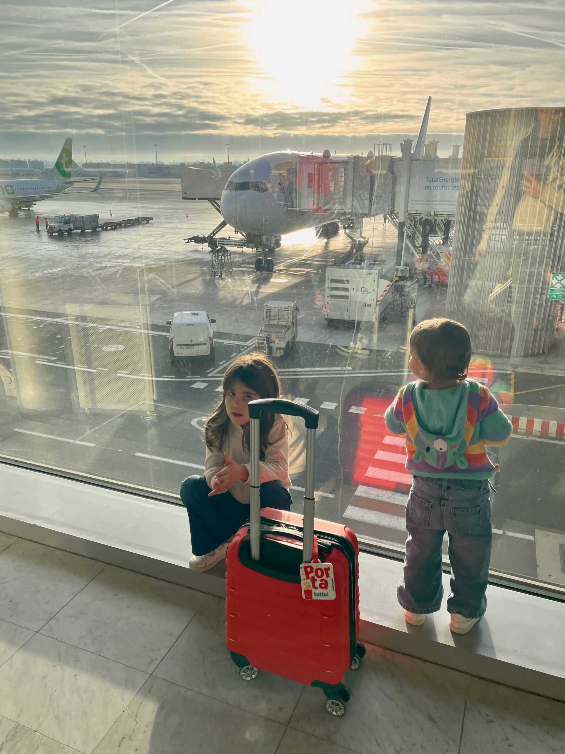 Le bambine guardano gli aerei dalla vetrata dell'aeroporto prima del volo per la Guadalupa